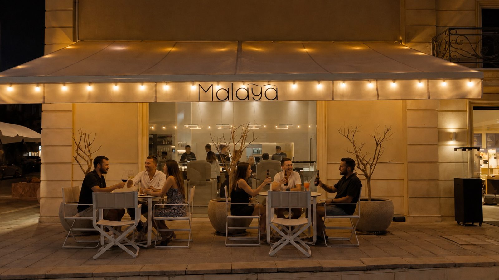 Malaya storefront at night — guests at outdoor tables under the lit awning